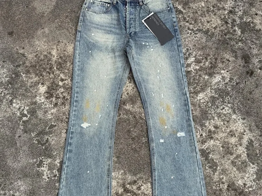 Light-wash straight-leg jeans with distressed knees, hung against a wall